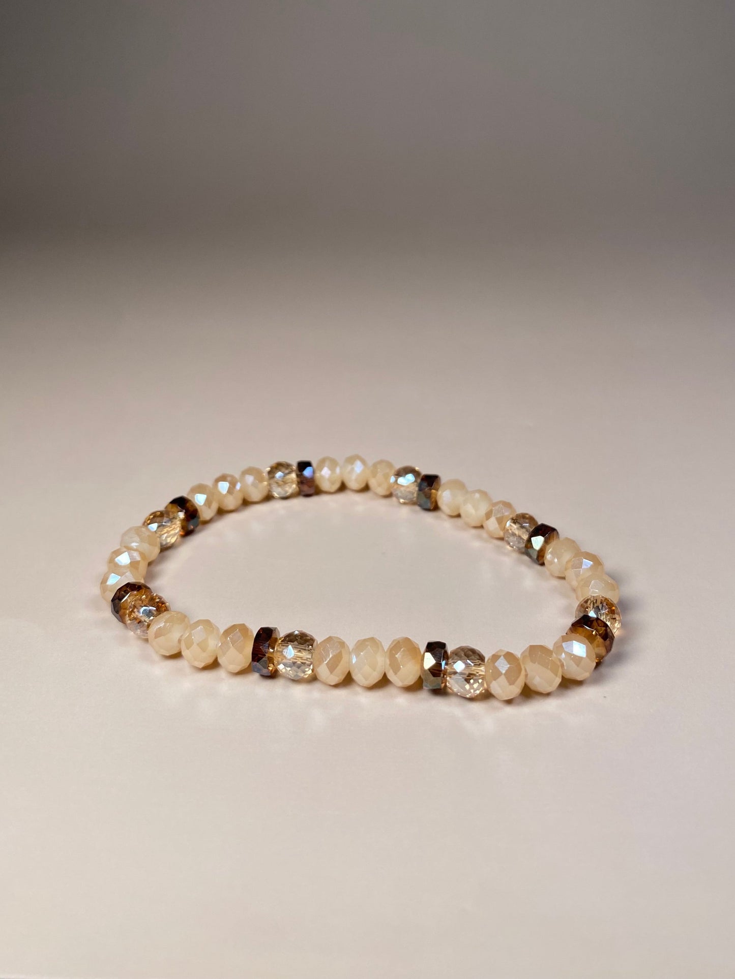 The Chelsea 6mm Cream Bracelet, featuring a harmonious blend of shiny opaque cream beads, accented by sparkly translucent and brown opaque beads, elegantly arranged in the center and radiating a captivating sparkle.
