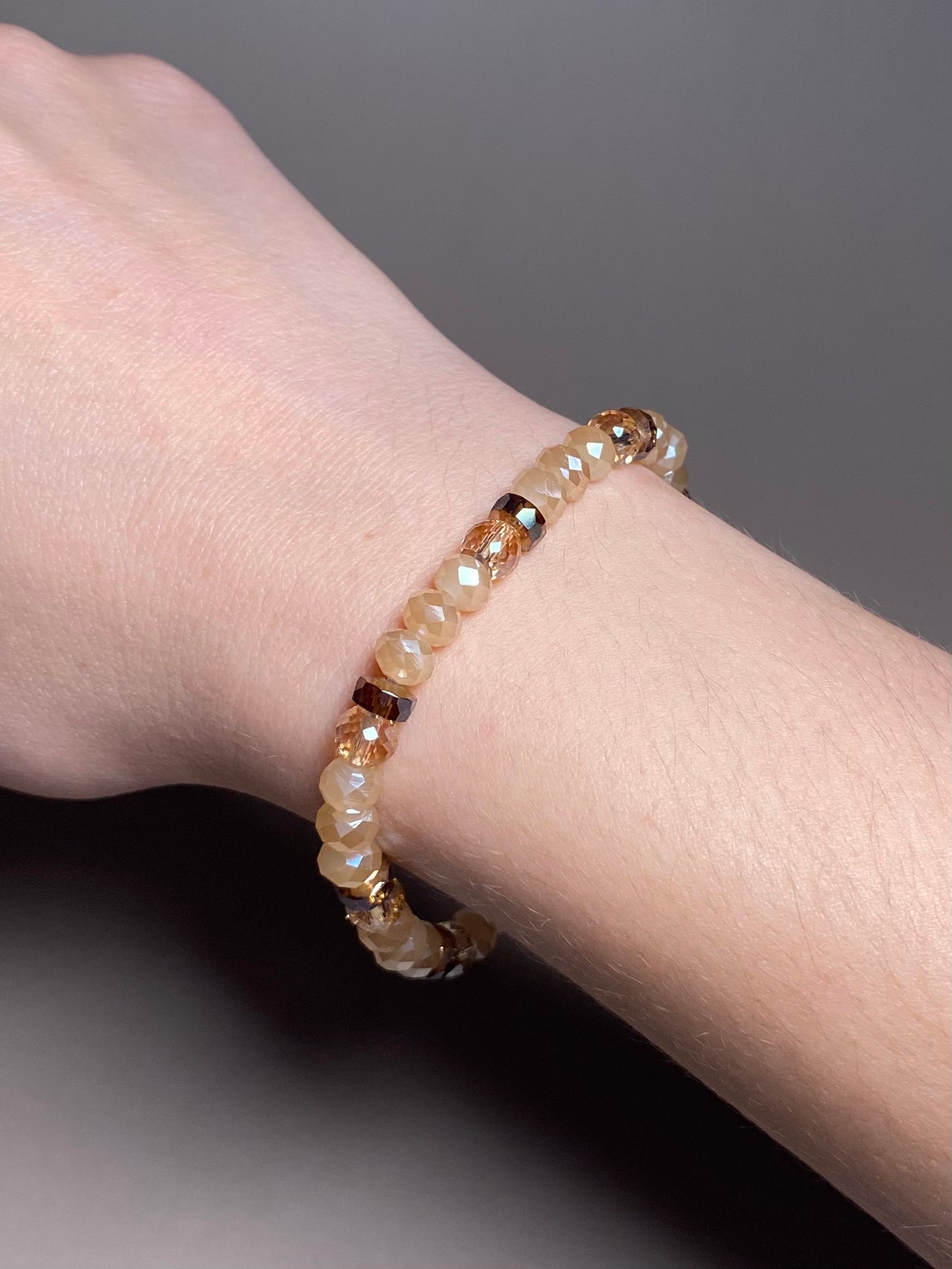 The Chelsea 6mm Cream Bracelet worn on a wrist, demonstrating its stylish and elegant design with a mix of shiny opaque cream and accent beads, perfect for enhancing any outfit.