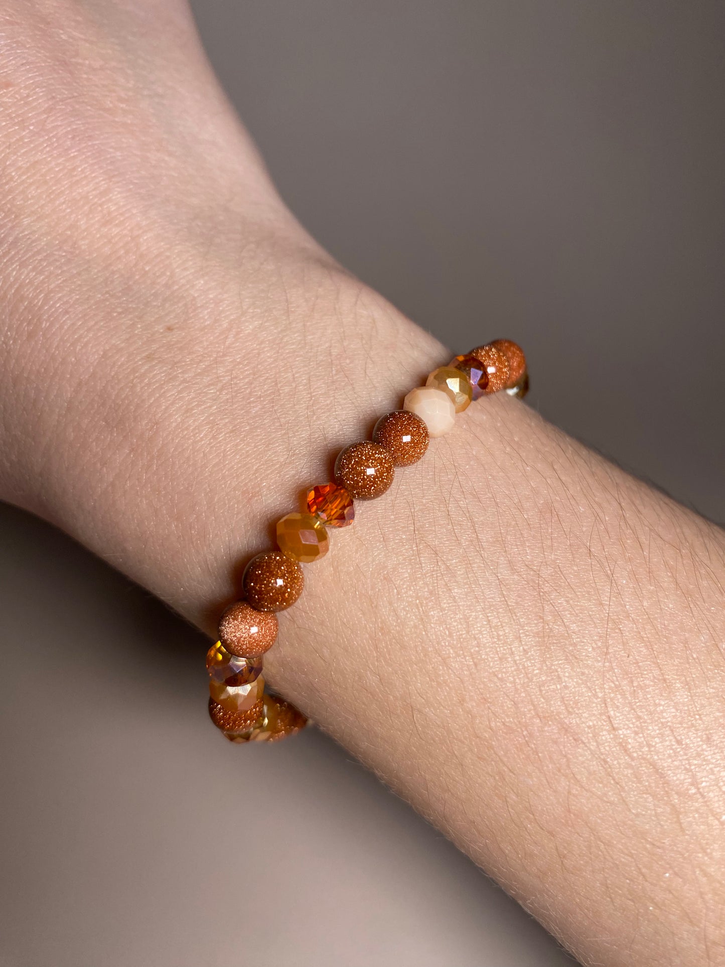The Francesca Moonstone 6mm Bracelet gracefully worn on a wrist, demonstrating its exquisite combination of goldstone and shiny gold/orange beads, adding a touch of glamour to any outfit.