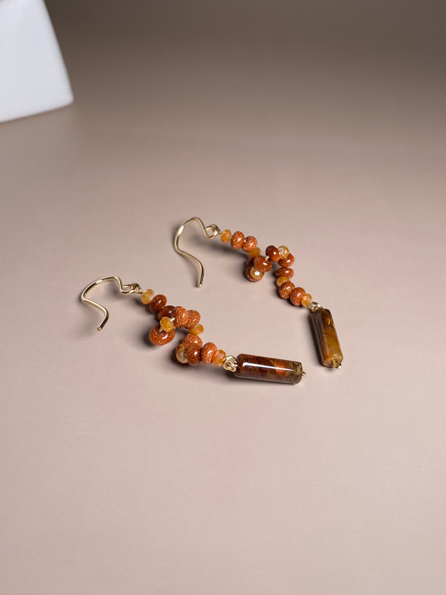 Francesca Moonstone Swirl Earrings featuring 3mm gold moonstone beads, swirling downwards with orange/gold 2mm glass beads and a pietersite bead elegantly dangling at the bottom. Designed with stylish gold-filled earring hooks and wire, the earrings sparkle in the center of the photo.