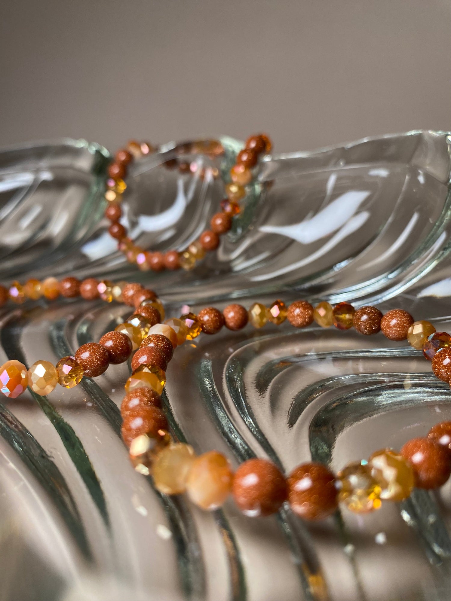 The Francesca Moonstone 6mm Bracelet beautifully displayed in a clear glass dish alongside two more of the same bracelet, highlighting their stunning goldstone beads and vibrant gold/orange accents.