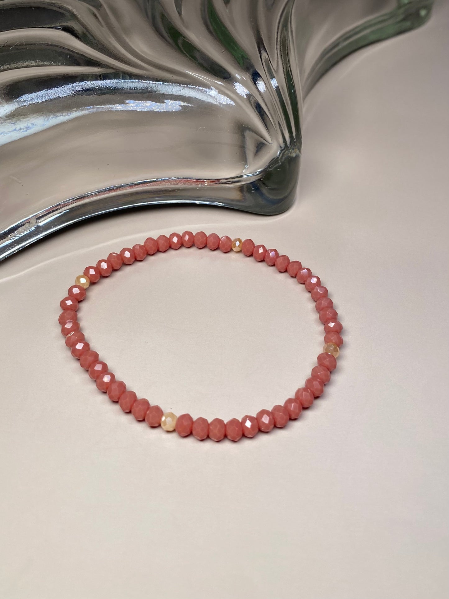 The Alice Dark Dusty Rose 5mm Bracelet, showcasing its dark dusty rose and cream beads, elegantly displayed in front of a stunning glass dish, highlighting its intricate design and shine.