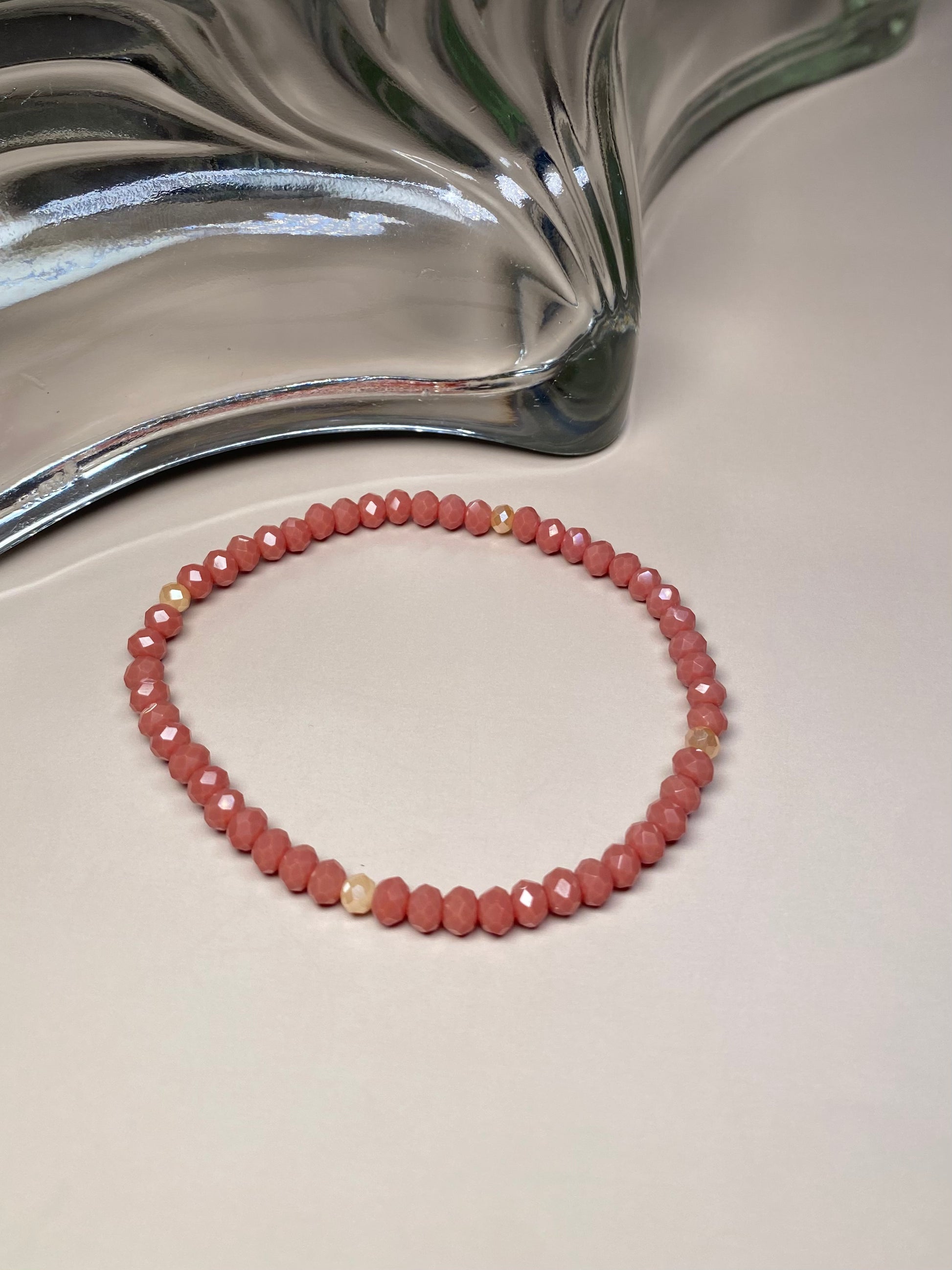 The Alice Dark Dusty Rose 5mm Bracelet, showcasing its dark dusty rose and cream beads, elegantly displayed in front of a stunning glass dish, highlighting its intricate design and shine.