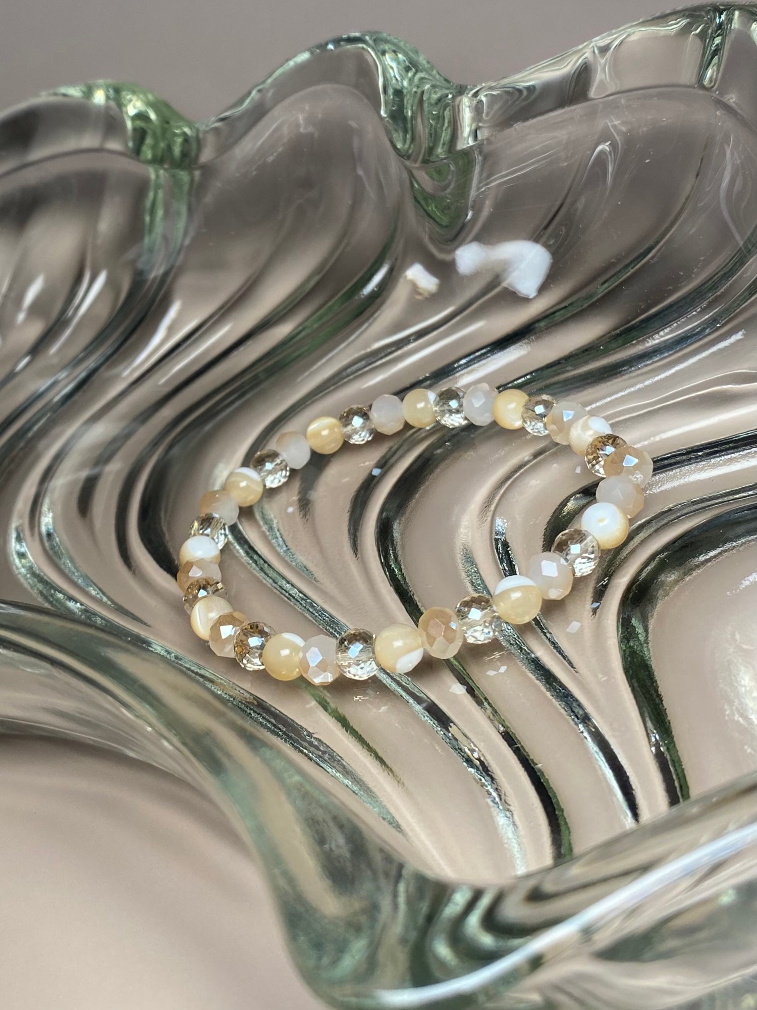 The Stella 6mm Mother of Pearl Sparkle Bracelet gracefully displayed in a gorgeous glass dish, highlighting its delicate mother of pearl and cream bead accents.