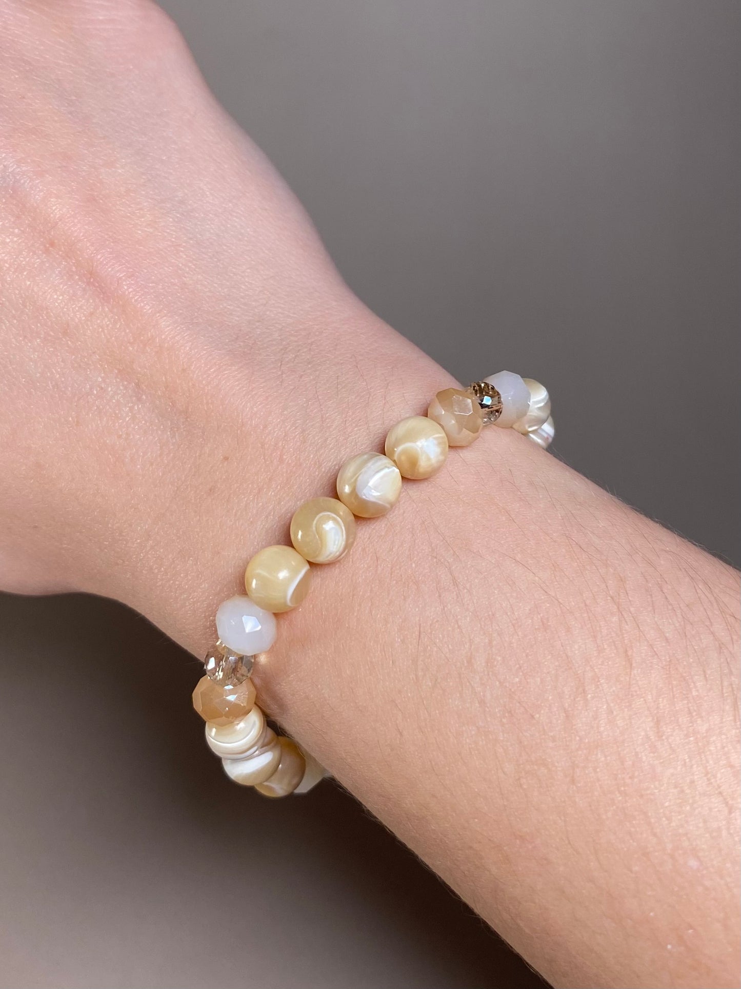The Stella 8mm Mother of Pearl Bracelet gracefully worn on a wrist, highlighting its exquisite blend of 8mm mother of pearl and cream beads.