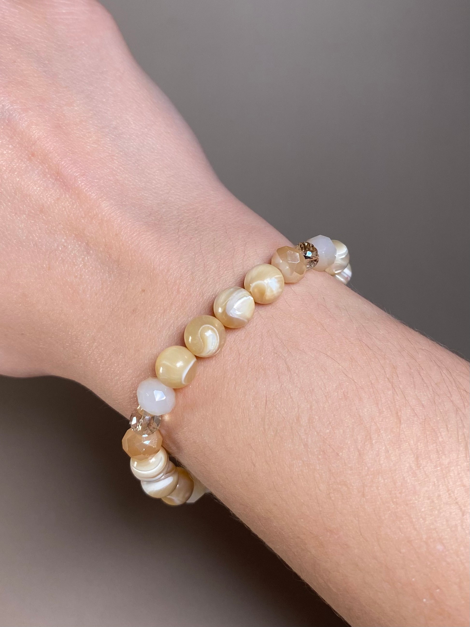 The Stella 8mm Mother of Pearl Bracelet gracefully worn on a wrist, highlighting its exquisite blend of 8mm mother of pearl and cream beads.