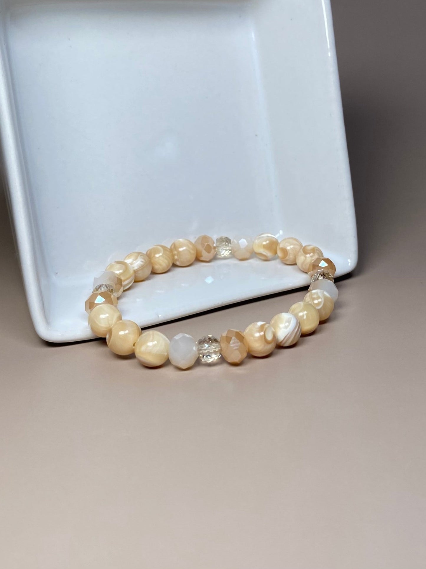 he Stella 8mm Mother of Pearl Bracelet elegantly positioned in front of a delicate porcelain dish, showcasing its combination of mother of pearl and shiny cream beads.