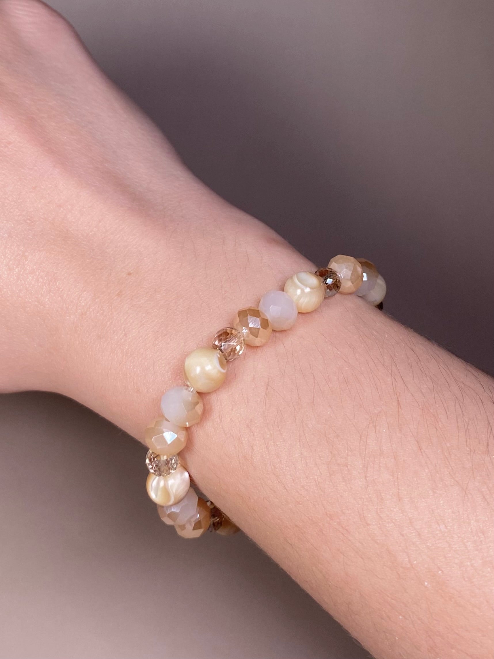 The Stella 8mm Mother of Pearl Bracelet gracefully worn on a wrist, highlighting its exquisite blend of 8mm mother of pearl and cream beads.